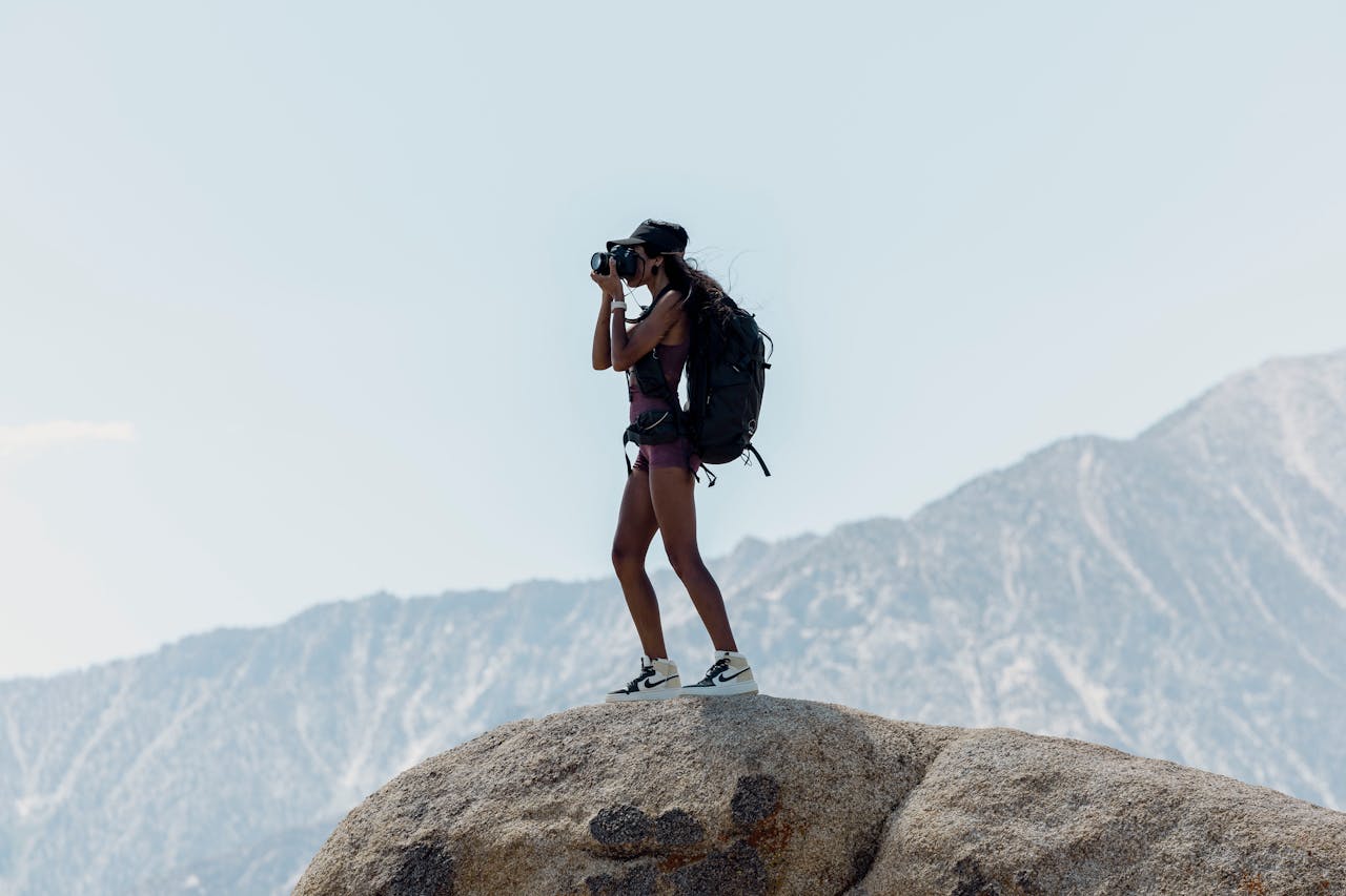 a-woman-standing-on-a-rock-in-mountains-and-taking-pictures-27081698